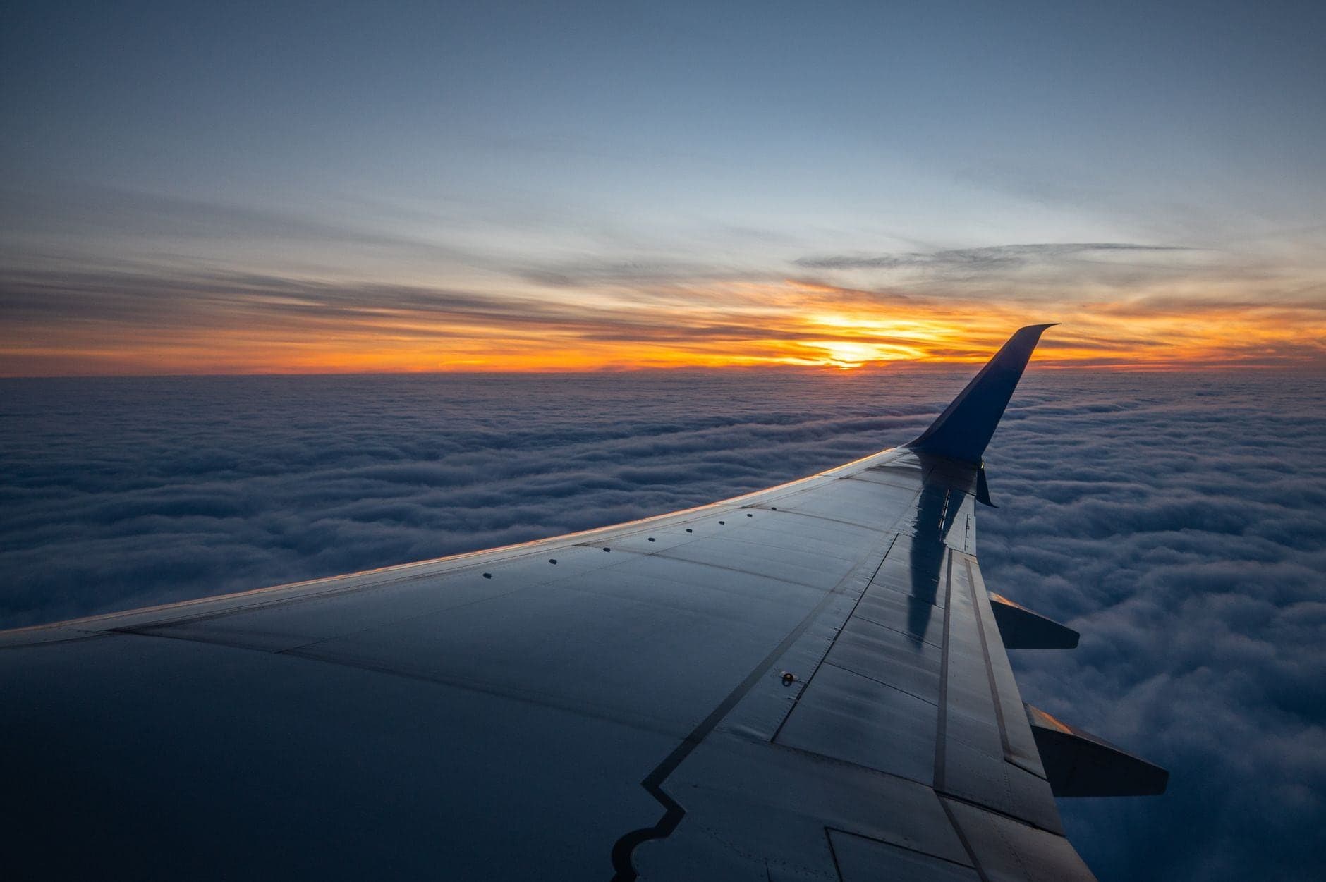Asa de avião sobre as nuvens no pôr do sol